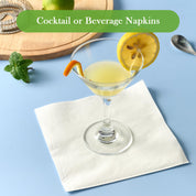 A refreshing cocktail in a glass garnished with lemon and orange slices, placed on a ECOLipak white napkin against a light blue background.