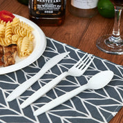 A white plastic knife, fork, and spoon are arranged beside a plate of pasta and grilled chicken on a patterned napkin.