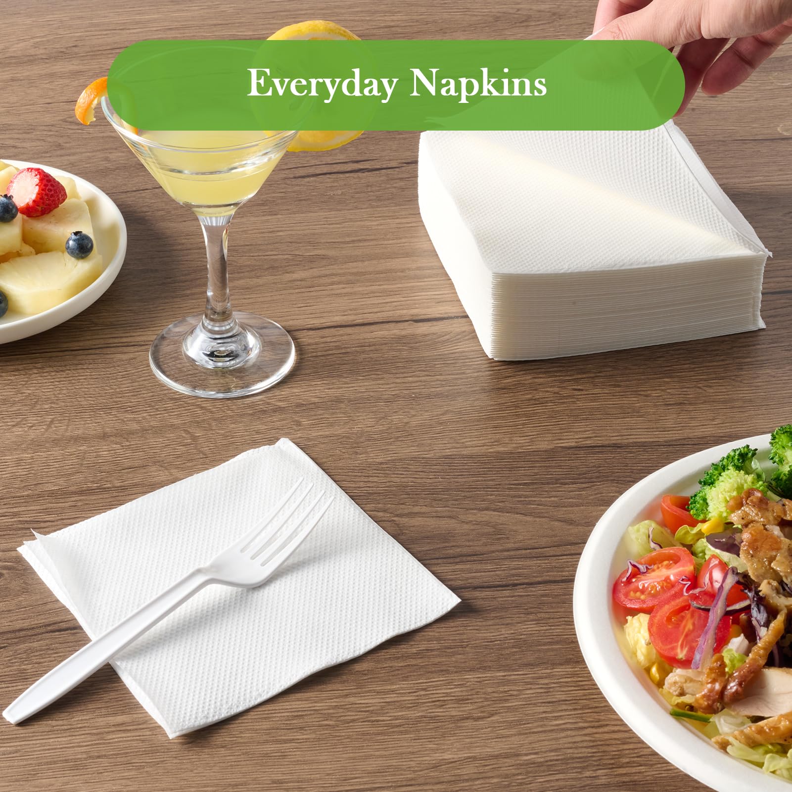 A table setting featuring a stack of ECOLipak white napkins, a cocktail with a lemon slice, a salad, and a fruit plate.