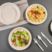 Two eco-friendly plates hold a salad with greens and a pasta dish with cherry tomatoes, accompanied by white disposable utensils.