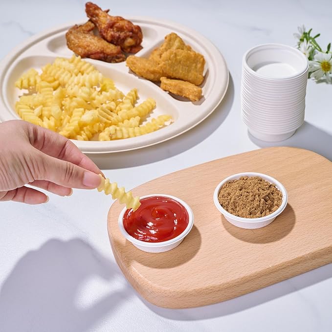 A hand dips a crinkle fry into ketchup, beside a wooden platter with brown sugar, a tray of chicken wings, and crinkle fries.