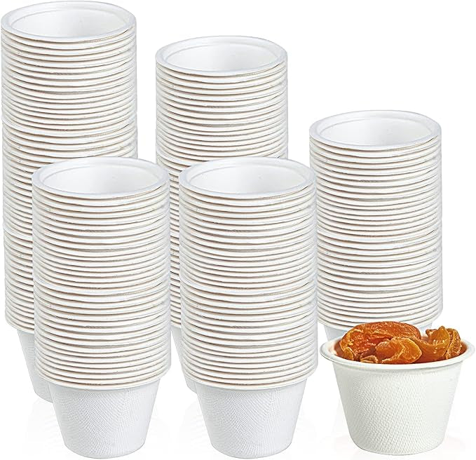 A stack of white paper cups with a gold rim, beside a small cup filled with dried apricots.