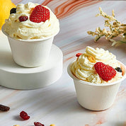 Two cups of creamy vanilla dessert topped with whipped cream, strawberries, and mixed berries on a marble background.