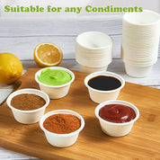 A selection of condiment cups on a wooden board with a lemon, featuring various sauces and spices, alongside stacks of empty cups.