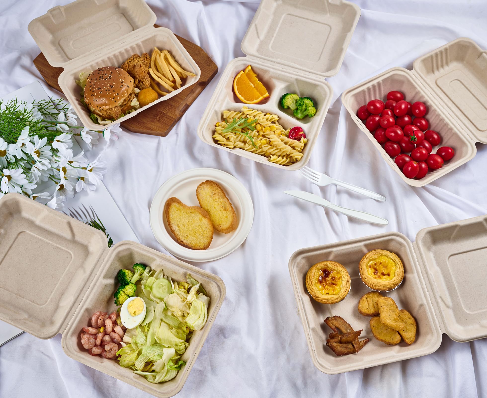 Assorted Ecolipak biodegradable meal containers with foods like burgers, pasta, salads, pastries and fruits, on a white cloth with cutlery and flowers.