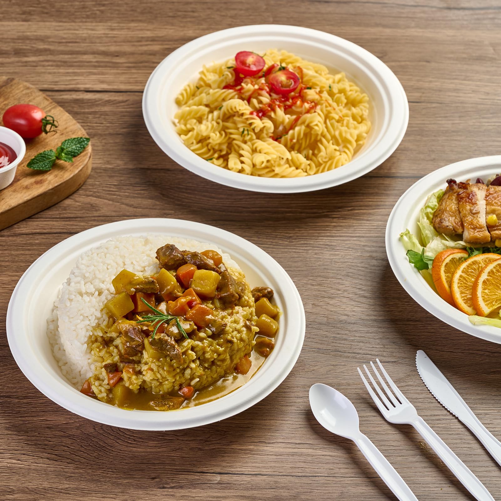 ECOlipak sugarcane pulp bowls hold various dishes like pasta, rice with curry, and a chicken - orange salad. CPLA - material knife, fork, and spoon, all eco - friendly, are placed beside on a wooden table. 